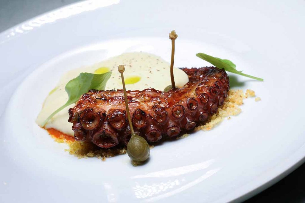 Polvo na brasa com molho da casa, espuma de alho-poró e batata com farofa de batata.  Foto: Inove Aceleradora