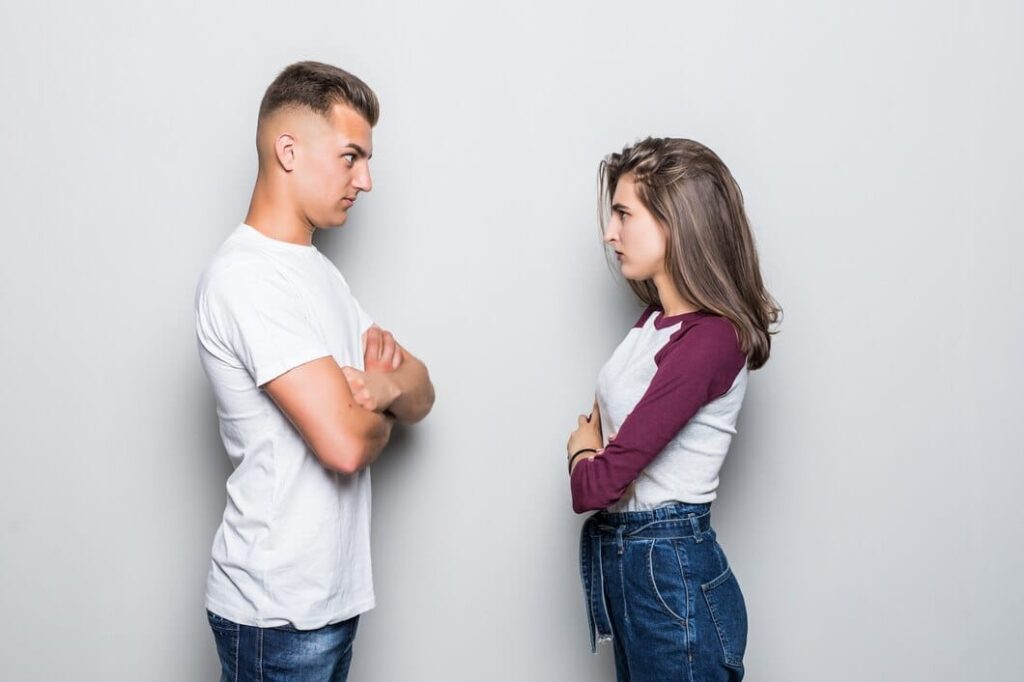 Casal em desentendimento. Homem e mulher de frente um para outro, com braços cruzados e cara fechada.