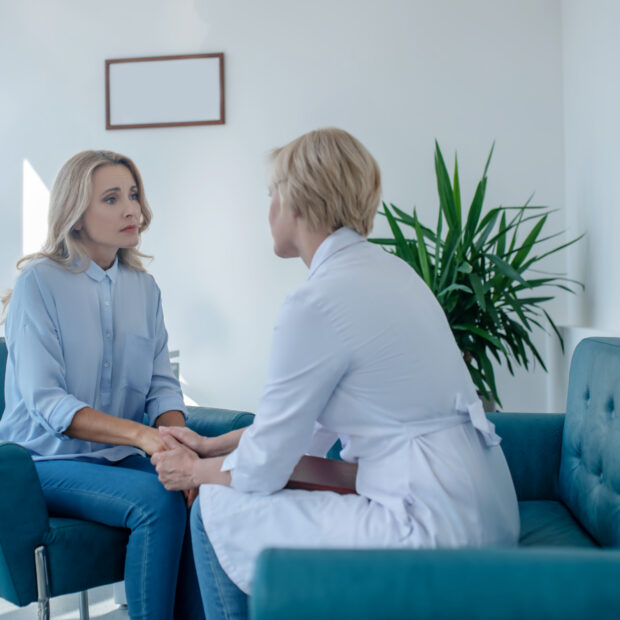 blonde female doctor soothing female patient, holding her hands