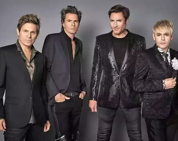 nick rhodes teclados john taylor baixo e roger taylor bateria e simon le bon de pe em frente a um muro olham para o lado 0.jpg
