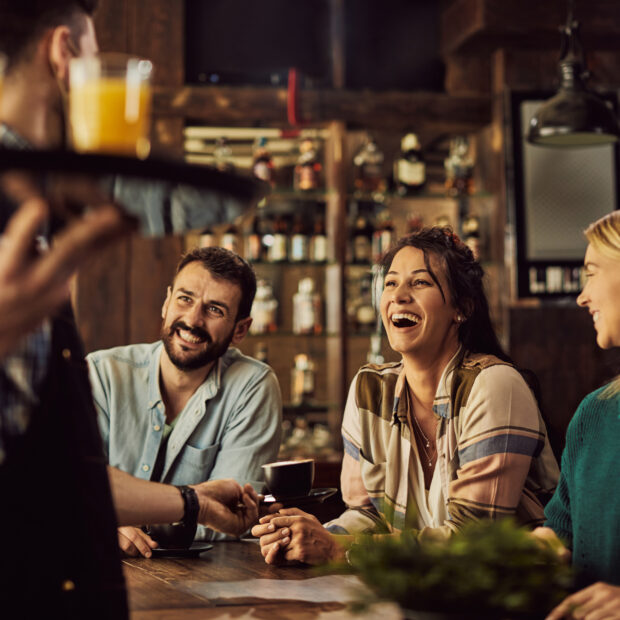 cheerful friends having fun while talking to a waiter in a cafe.