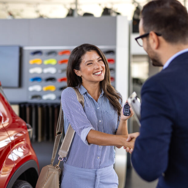 beautiful young woman is talking to handsome car dealership worker while choosing a car in dealership
