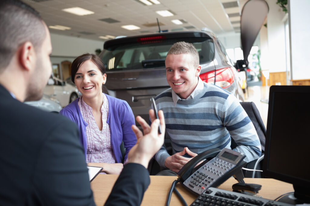 couple smiling while talking with a salesman in a car shop