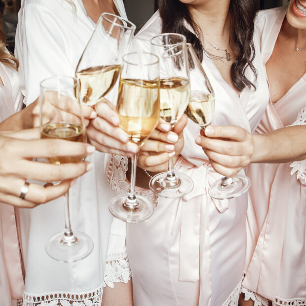 bride and bridesmaids stand in silk robes with glasses of champa