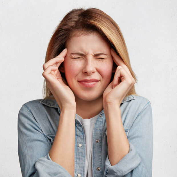 indoor shot of depressed female model wears denim jacket, keeps finger on temples, suffers from headache, feels pain, being overworked, need rest and calm. people, tiredness, exhaustion concept