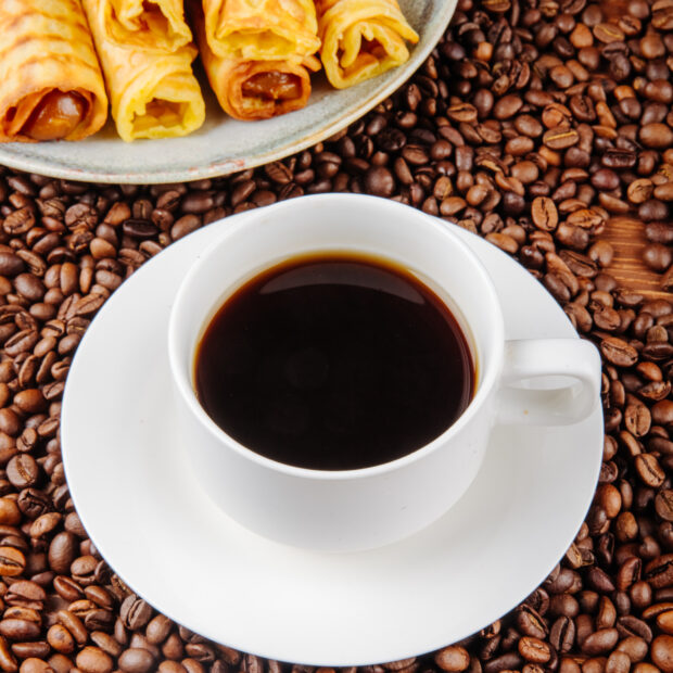 side view of a cup of coffee with wafer roll filled with condensed milk on a plate on coffee beans background cafe
