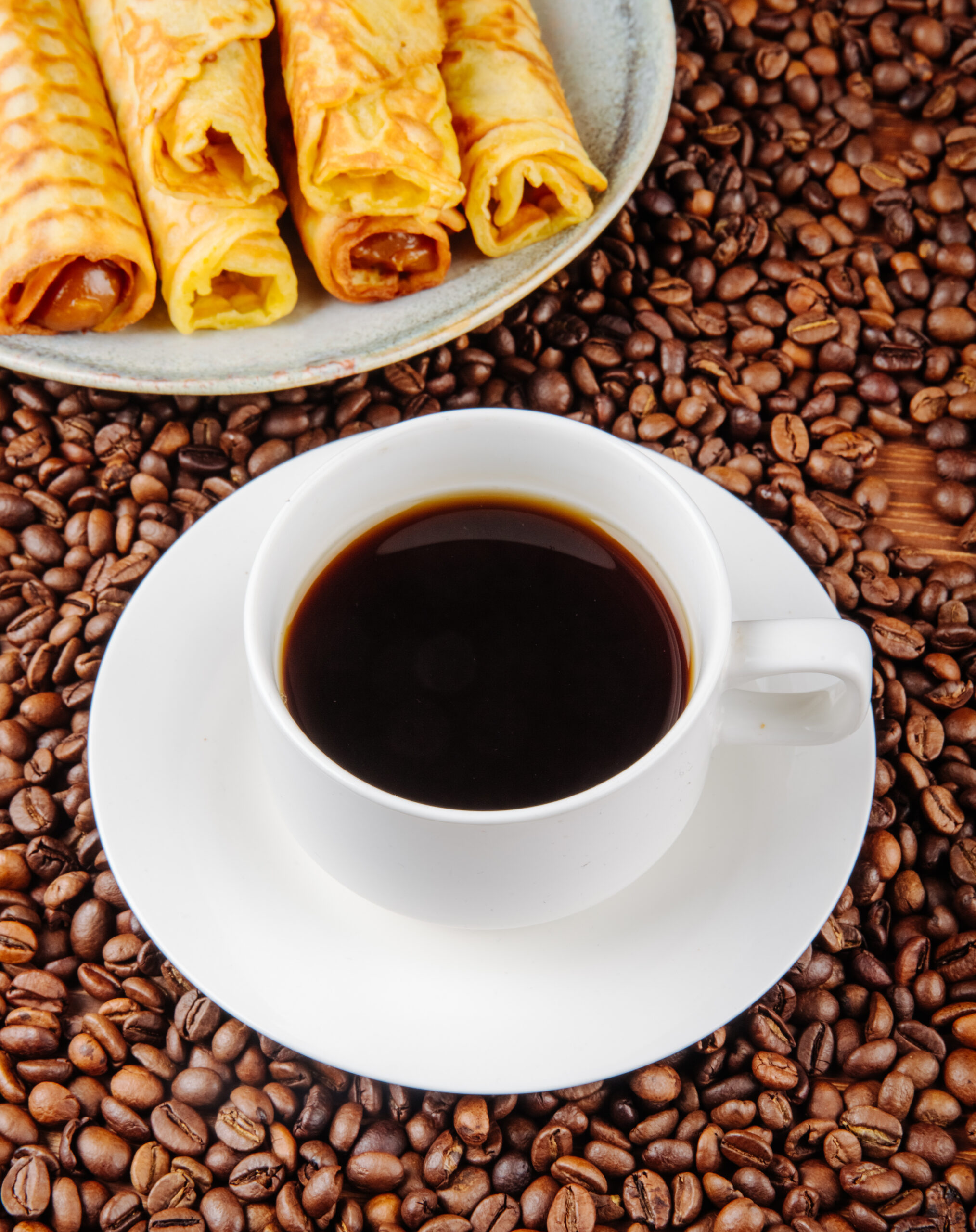 side view of a cup of coffee with wafer roll filled with condensed milk on a plate on coffee beans background cafe
