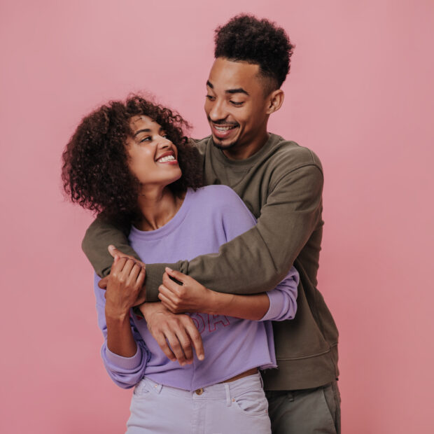 couple in love looking at each other with love and smiling on pink background. charming man in brow
