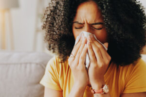 sofa, woman and sick with tissue for blowing nose, allergy and inflammation of sinus in living room. home, female person and medical virus with sneezing for influenza, cold and illness on couch