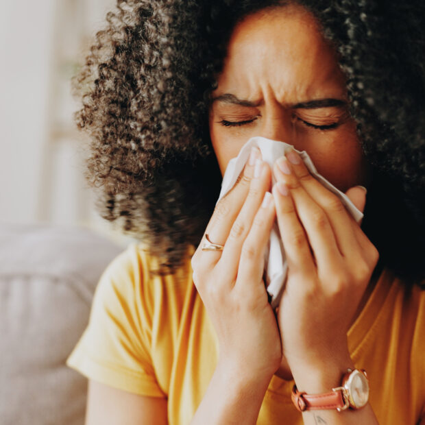 sofa, woman and sick with tissue for blowing nose, allergy and inflammation of sinus in living room. home, female person and medical virus with sneezing for influenza, cold and illness on couch