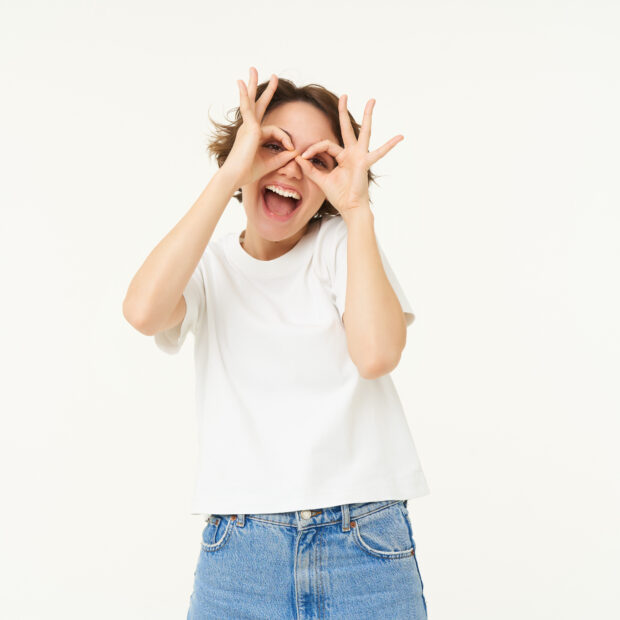 portrait of carefree european woman, showing glasses with hands over eyes and smiling, posing over white background