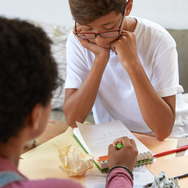 education, teaching and learning concept. older sister explains how make task to brother who studies at school, points at notes in spiral diary, sit in coworking space. training teacher and student