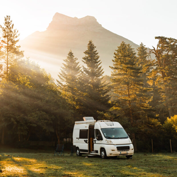 camper van in a valley with amazing landscape views of forest, mountains and sun rays during sunrise. van road trip holiday and outdoor summer adventure. nomad lifestyle concept
