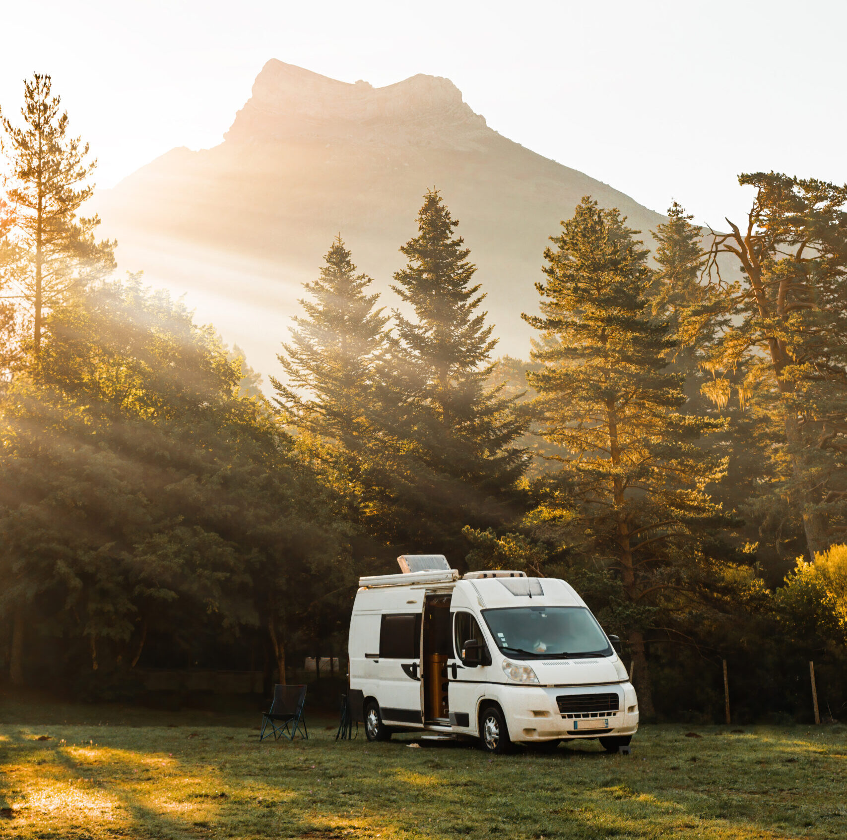 camper van in a valley with amazing landscape views of forest, mountains and sun rays during sunrise. van road trip holiday and outdoor summer adventure. nomad lifestyle concept