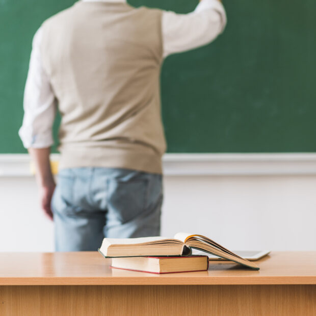math teacher writing chalkboard near table with books