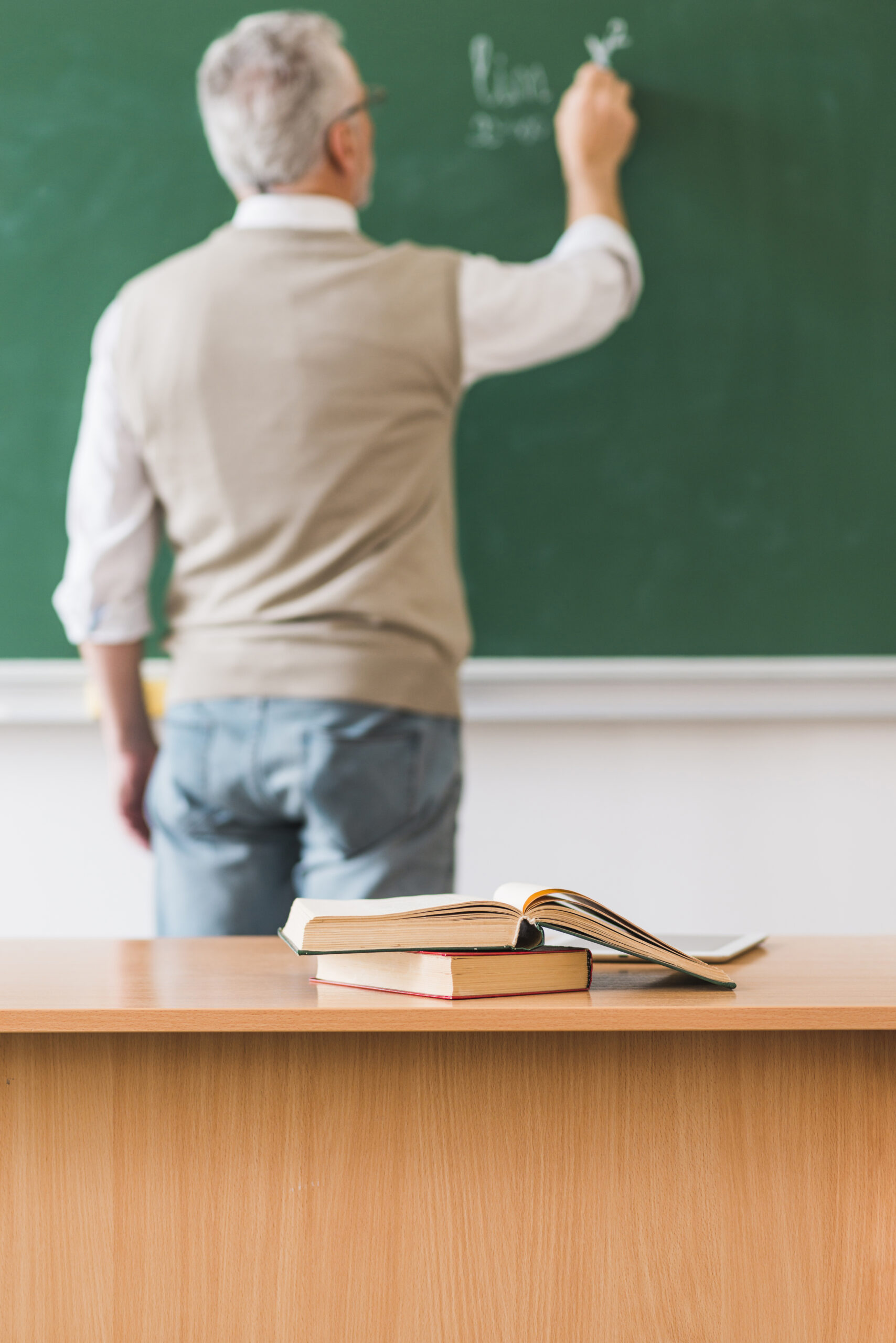 math teacher writing chalkboard near table with books