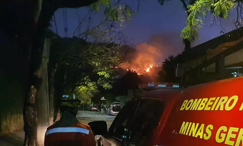 imagem mostra parta da lateral do carro do corpo de bombeiros militar da corporacao aparece de costas ao lado do carro ao fundo e possivel ver o fogo na serra 2 52361