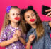 pleased little pretty girls holding fake lips on sticks taking selfie isolated on pink background with copy space
