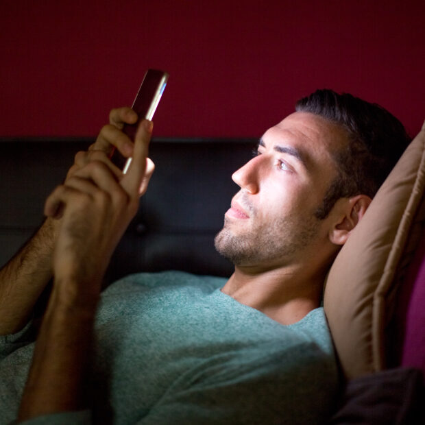 focused man using smartphone on sofa at night