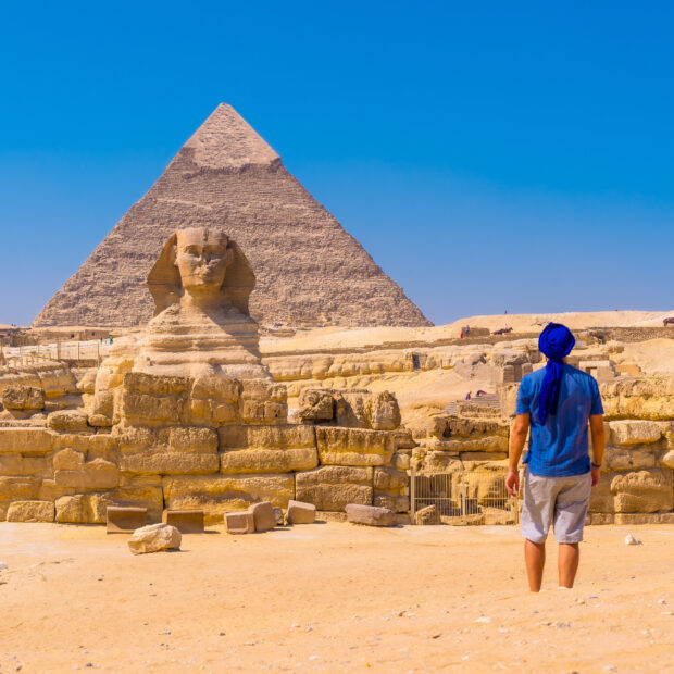 young man walking towards the great sphinx of giza and in the background the pyramid of khafre,