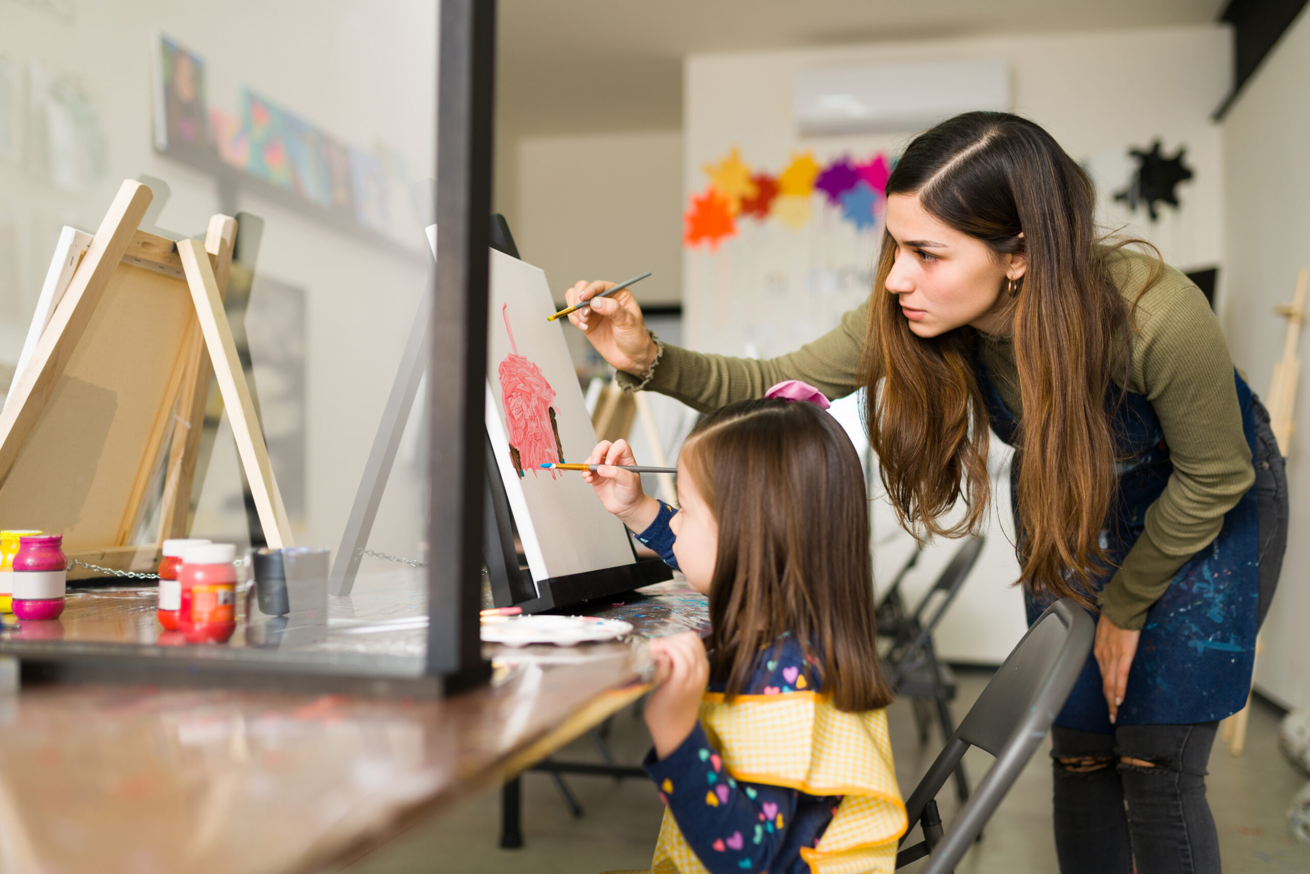 side view of a female instructor helping a girl kid to finish her artwork