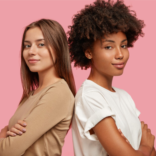 diversity and feminity concept. confident young mixed race women stand backs to each other, keep hands crossed over chest, collaborate for common task, dressed casually, isolated over pink background.