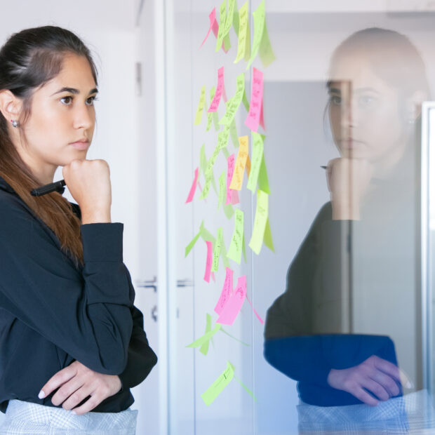 thoughtful latin businesswoman holding marker and reading notes