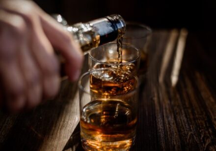 despejando bebida forte de alcool nos copos que estao sobre mesa de madeira 696x465