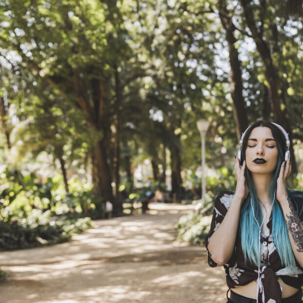 woman with tattoo her hand enjoying music headphone standing park.jpg