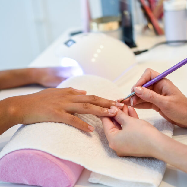 close up of beautician painting a woman's nails with a brush in