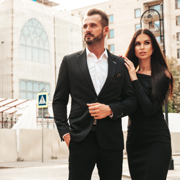 beautiful fashion woman and her handsome elegant boyfriend in suit. sexy brunette model in black evening dress. fashionable couple posing in the street in europe. brutal man and his female outdoors