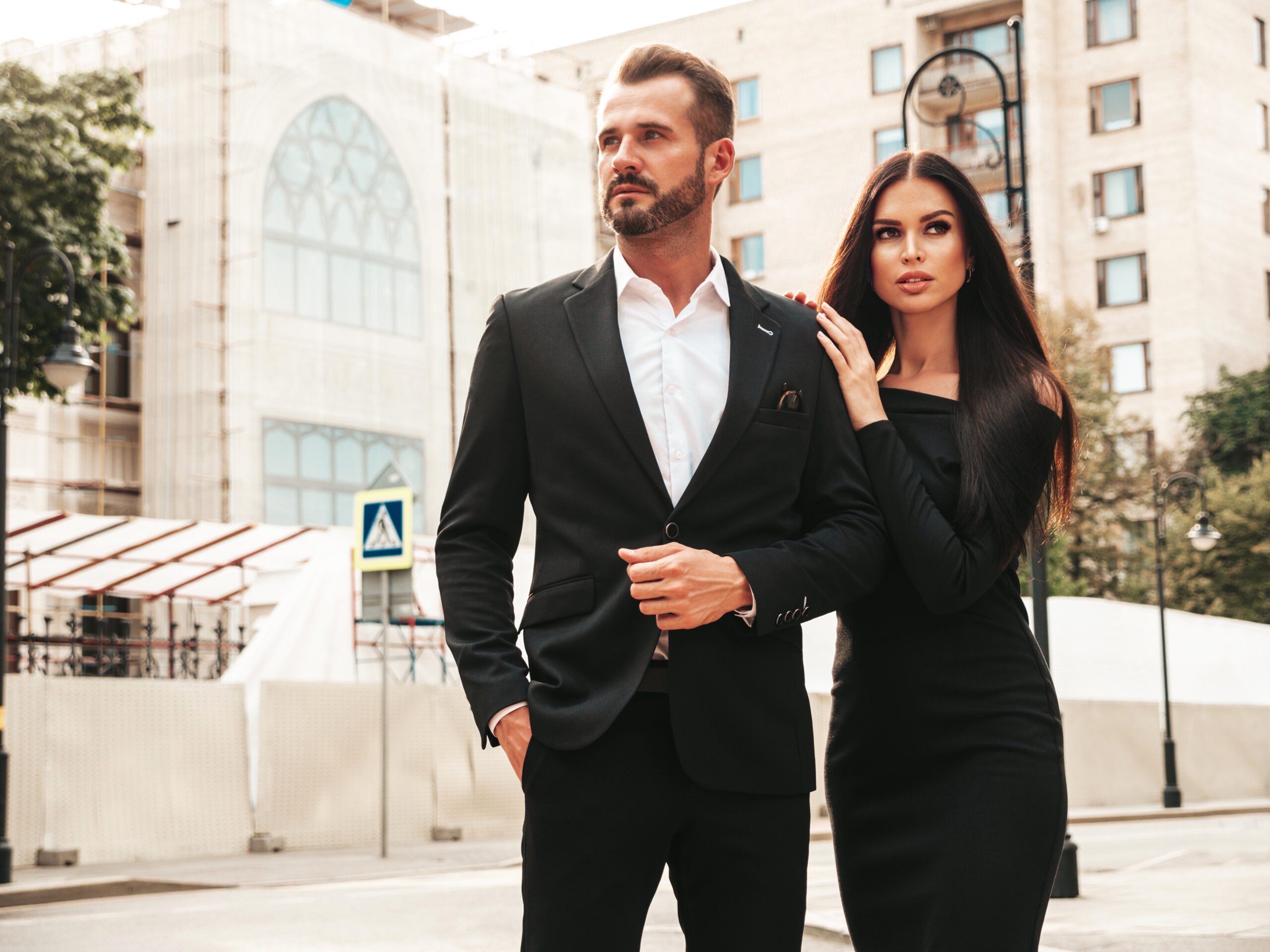 beautiful fashion woman and her handsome elegant boyfriend in suit. sexy brunette model in black evening dress. fashionable couple posing in the street in europe. brutal man and his female outdoors