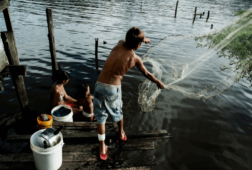 Moradores às margens de um rio, com um homem lançando uma rede de pesca em área ribeirinha — Autor: Guilherme Bergamini