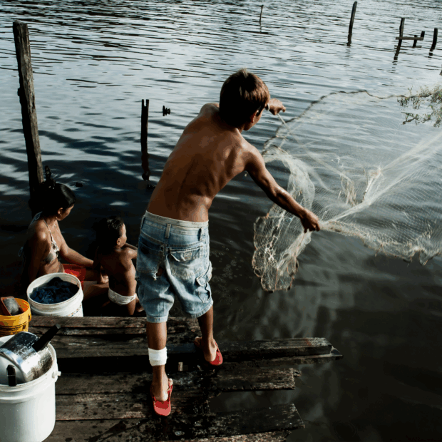 Moradores às margens de um rio, com um homem lançando uma rede de pesca em área ribeirinha — Autor: Guilherme Bergamini
