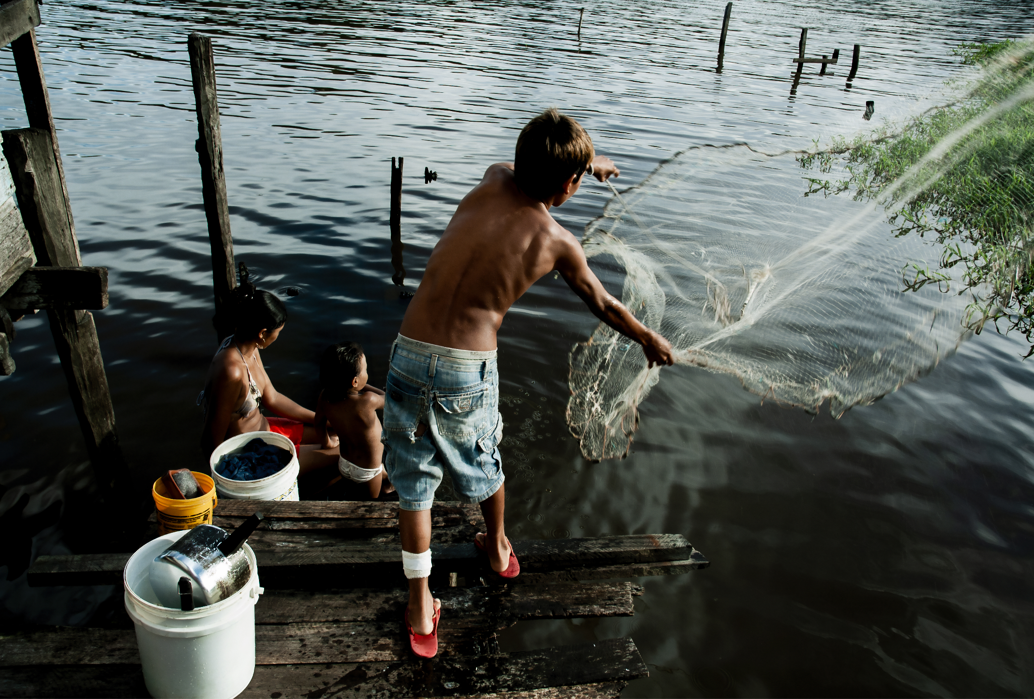 Moradores às margens de um rio, com um homem lançando uma rede de pesca em área ribeirinha — Autor: Guilherme Bergamini