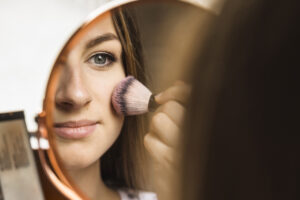 hand mirror with reflection woman applying blusher her face