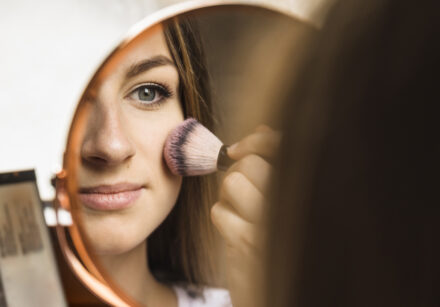 hand mirror with reflection woman applying blusher her face
