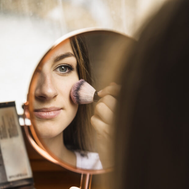 hand mirror with reflection woman applying blusher her face