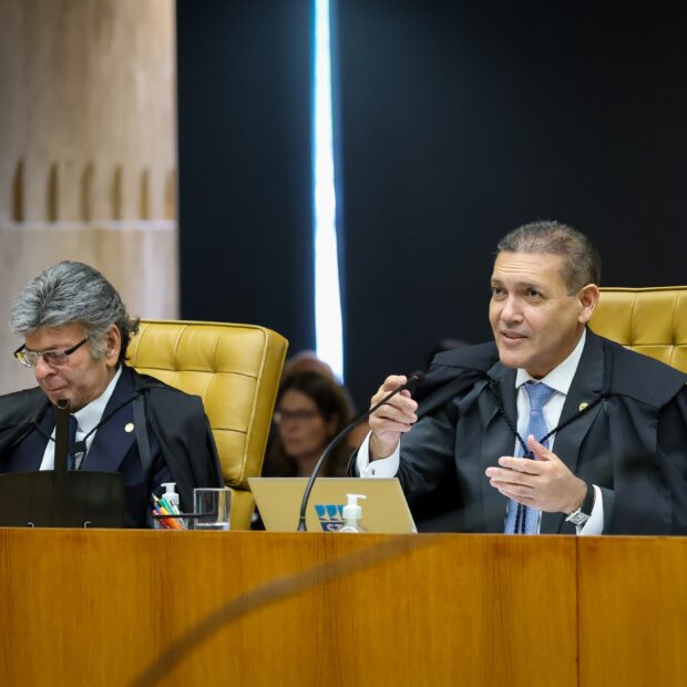 Dois homens com trajes judiciais sentados à mesa em uma sessão de tribunal, com um deles gesticulando enquanto fala. Na foto: Nunes Marques.