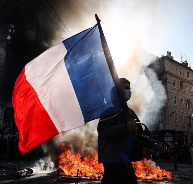 116633921 topshot a protester waving a french national flag walks past a fire during clashes prior
