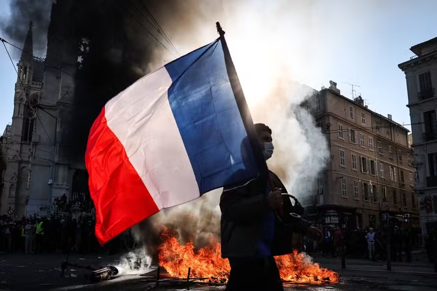 116633921 topshot a protester waving a french national flag walks past a fire during clashes prior