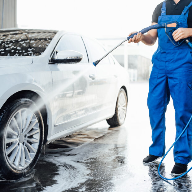 professional washer blue uniform washing luxury car with water gun open air car wash
